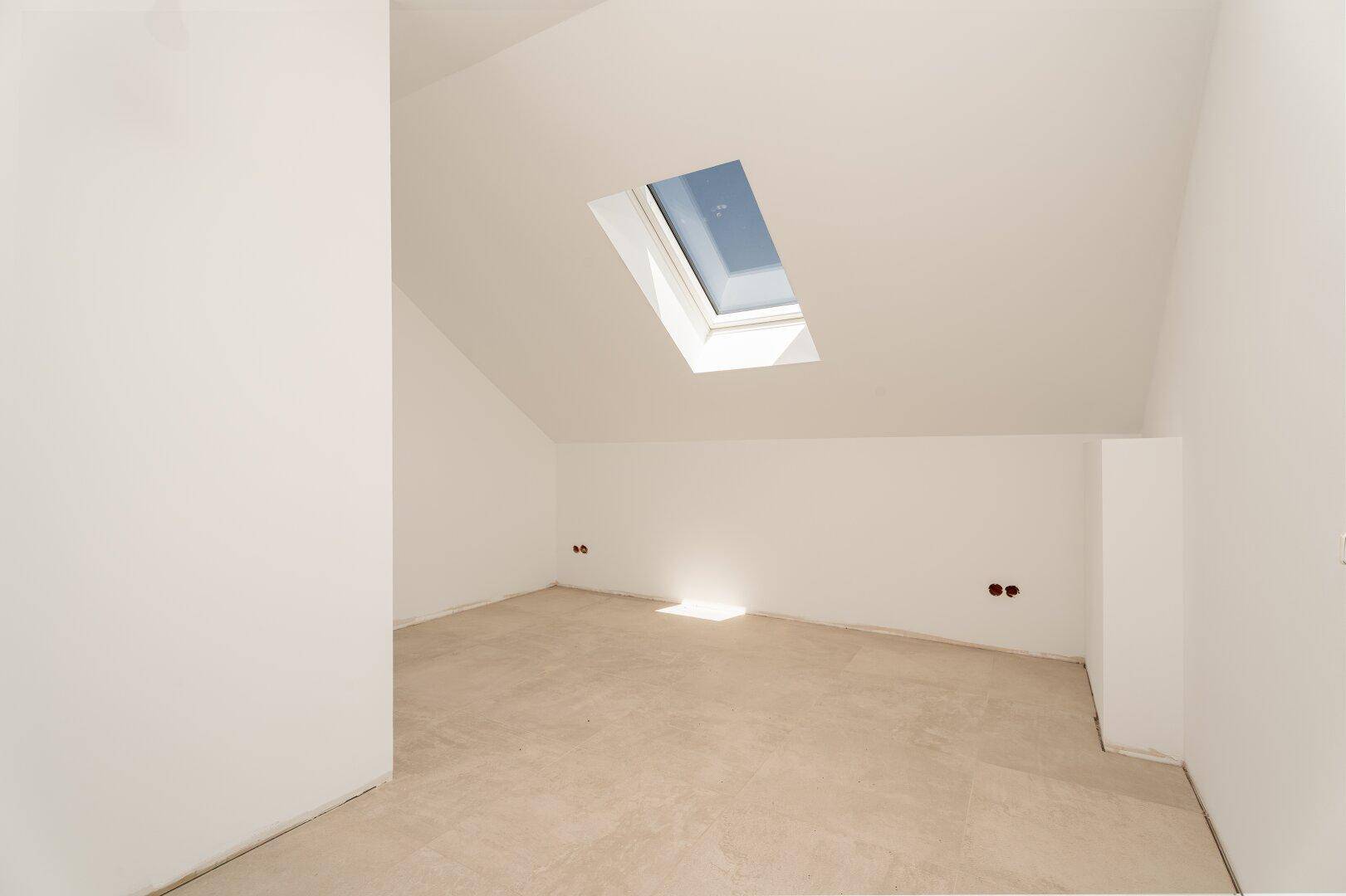 Dachbodenraum mit schrägen Wänden und einem Dachfenster, das viel Licht spendet.