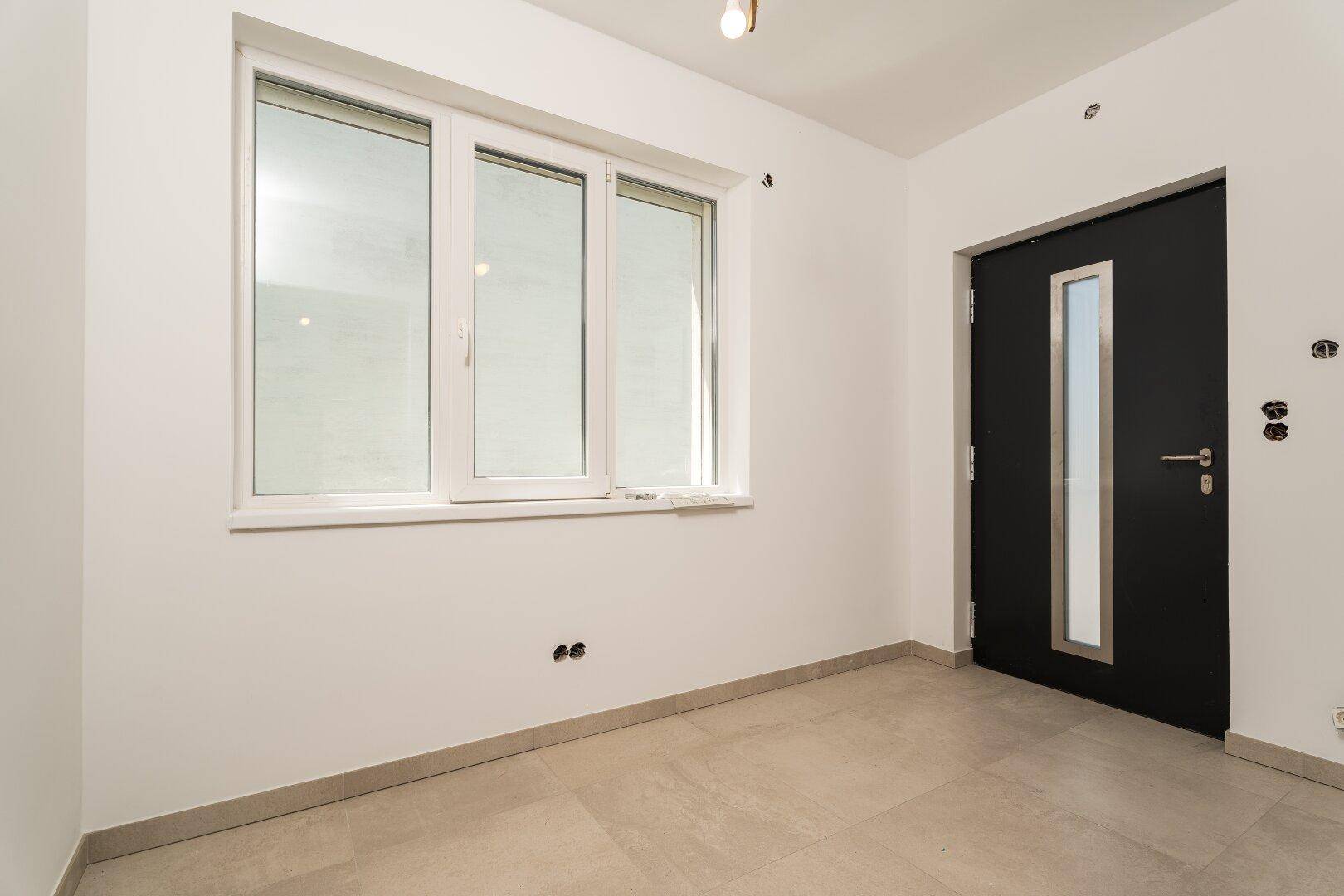 Heller Eingangsbereich mit Fliesenboden, großem Fenster und moderner Haustür.