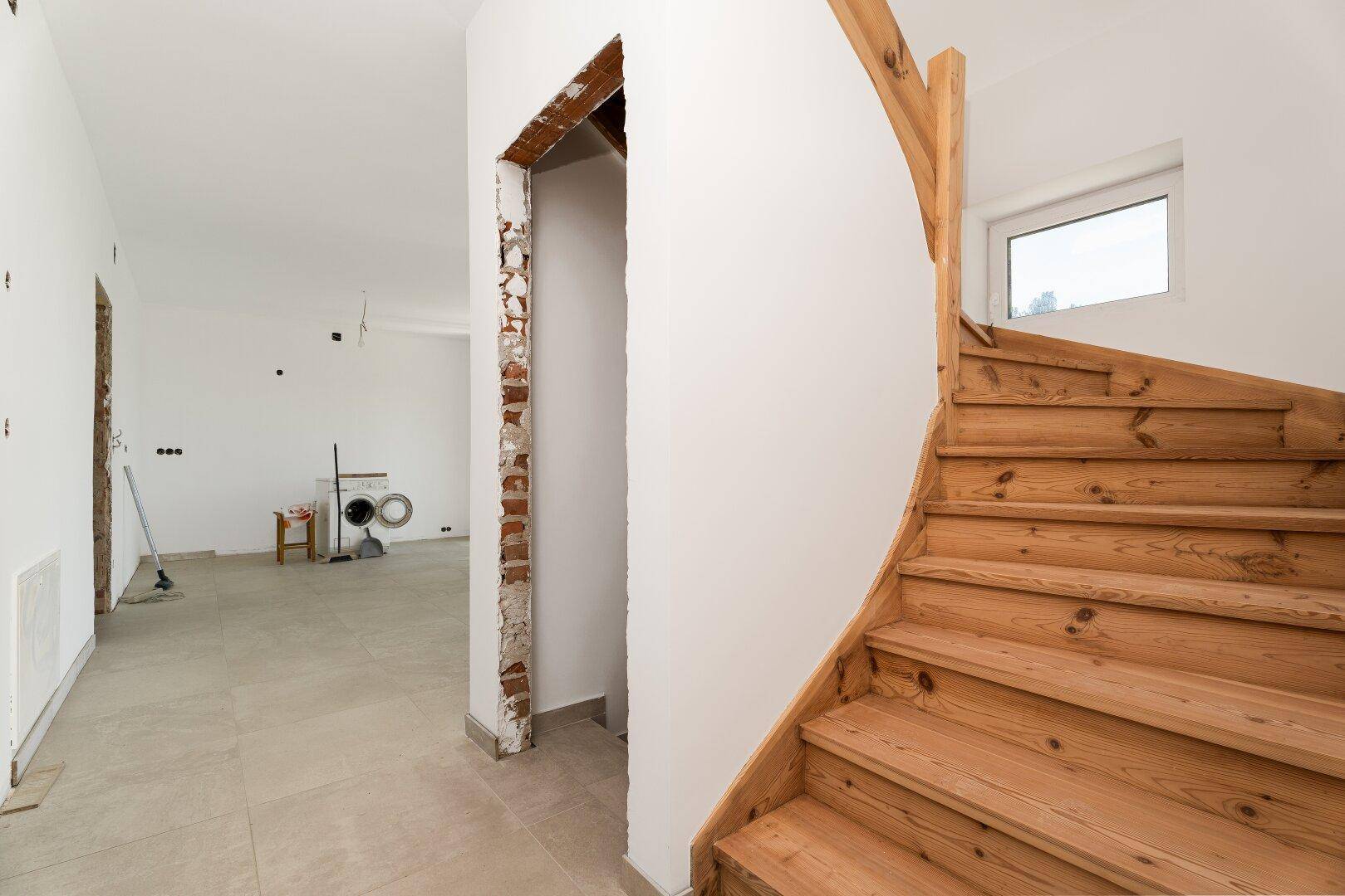 Heller Flur mit einer eleganten Holzwendeltreppe und Blick in einen weiteren Raum.