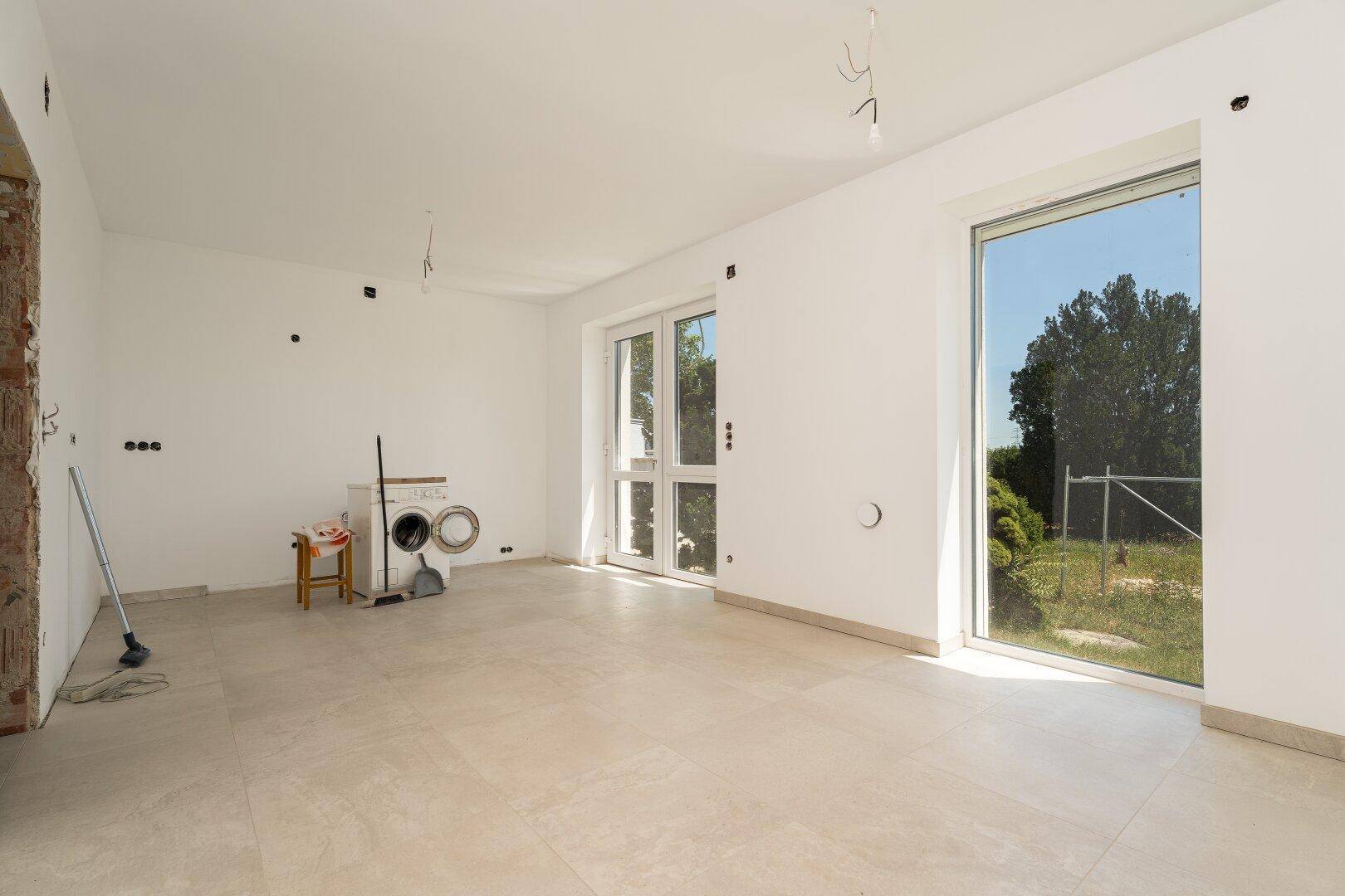 Großer, heller Wohnraum mit Fliesenboden, Zugang zum Garten und viel Tageslicht.