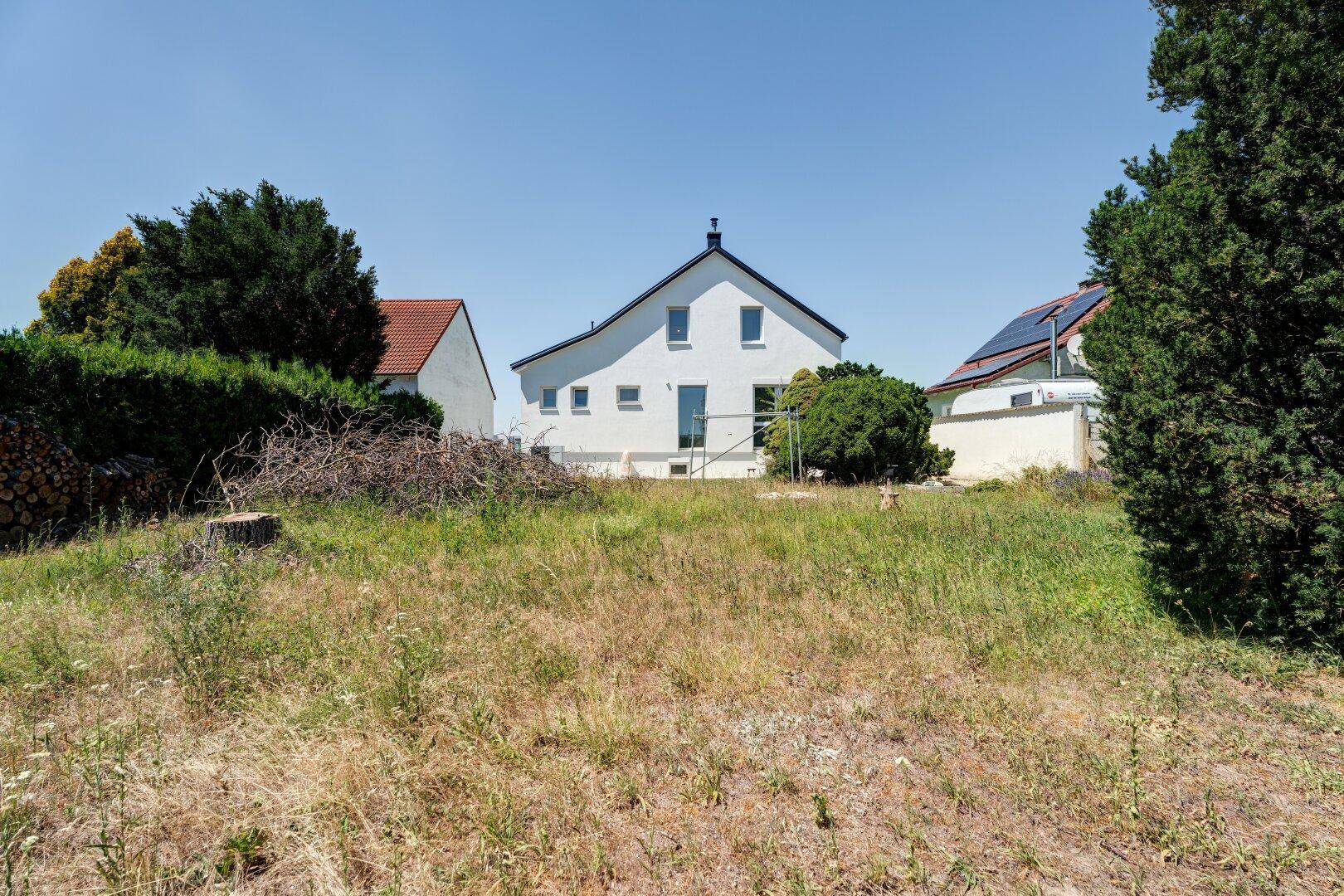 Rückansicht des weißen Hauses mit Blick auf den ungepflegten Garten und die umliegende Natur.