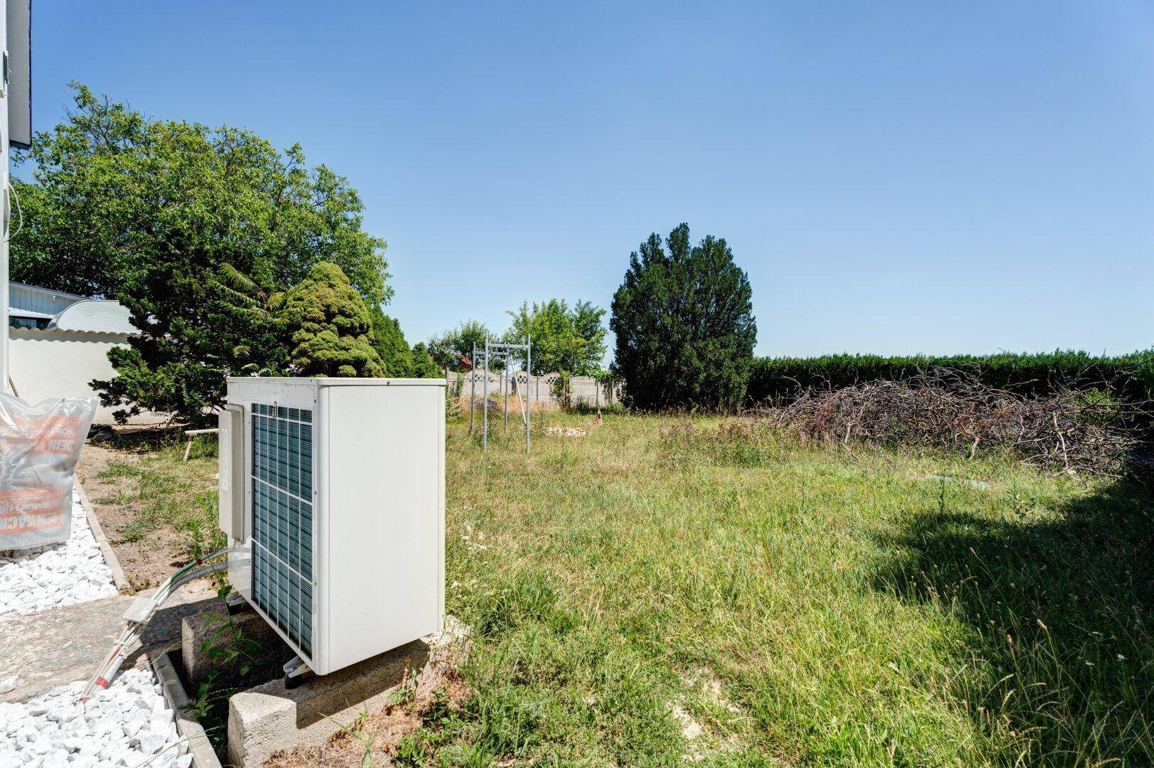 Ungepflegter Gartenbereich mit einer Außeneinheit der Klimaanlage und viel Grün.