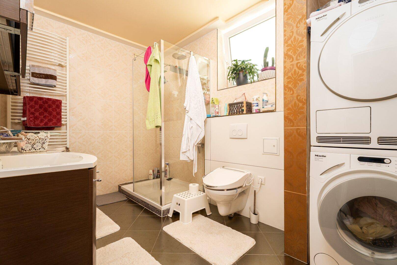 Modernes Badezimmer mit Duschkabine, WC, Waschbecken und integrierter Waschmaschine und Trockner.