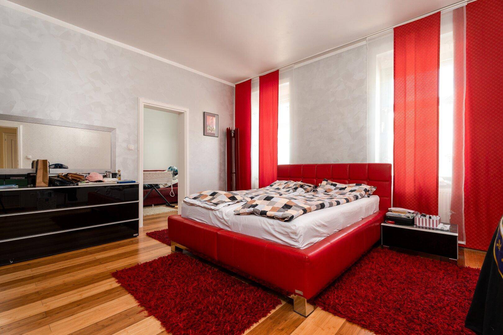 Schlafzimmer mit rotem Bett, Holzfußboden und farblich passenden Vorhängen.