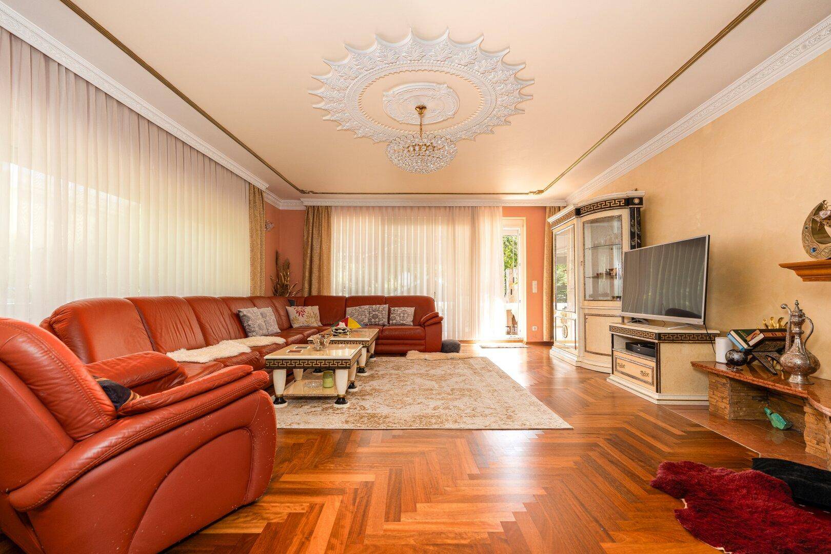 Geräumiges Wohnzimmer mit roten Ledersofas, Fischgrätparkett und dekorativer Stuckdecke.