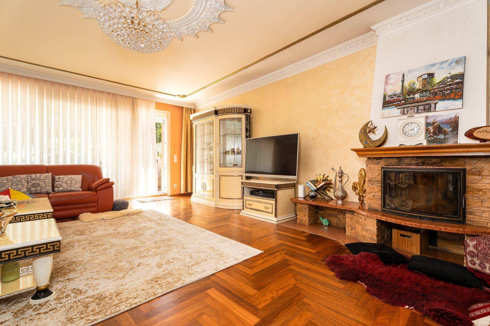 Gemütliches Wohnzimmer mit Kamin, roten Ledersofas und elegantem Fischgrätparkett.