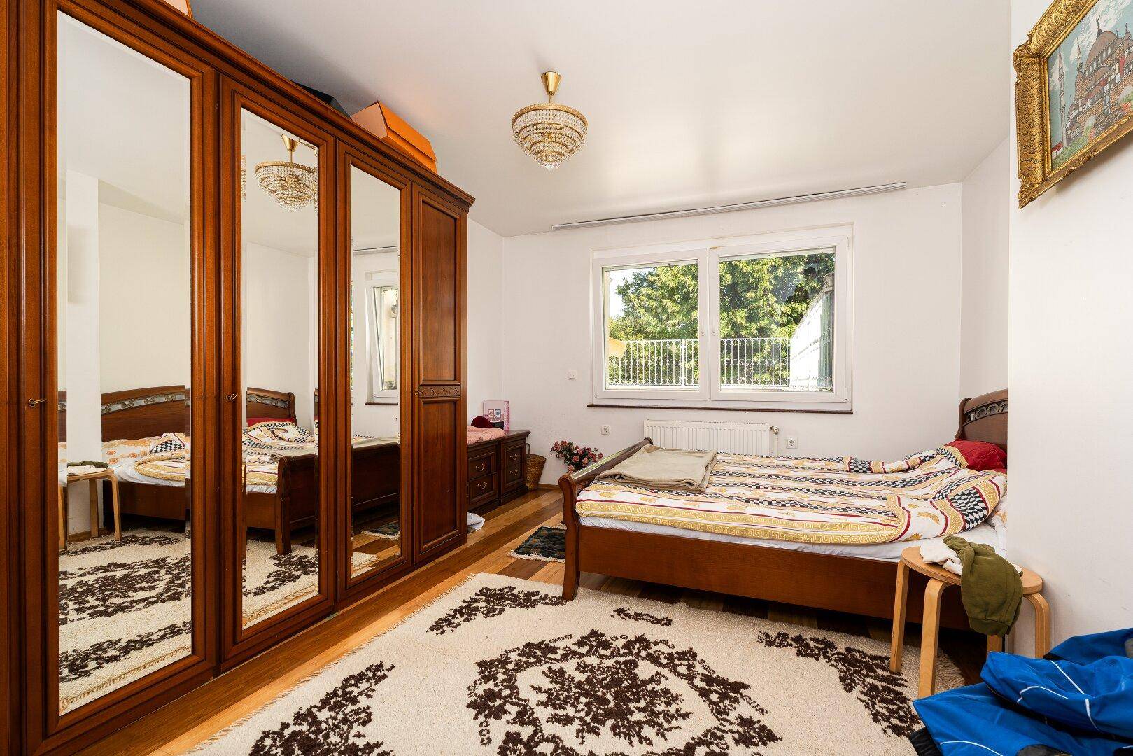 Schlafzimmer mit Holzbett, großem Spiegelschrank und gemustertem Teppich.