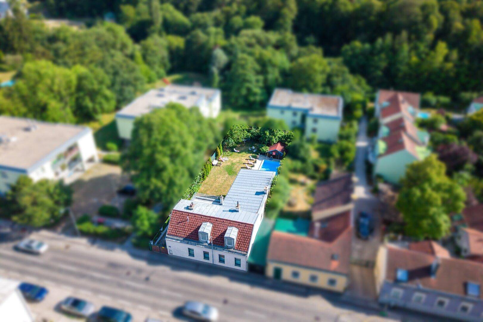 Luftaufnahme eines Wohnhauses mit Mansarddach, langem Garten und Swimmingpool in städtischer Umgebung.
