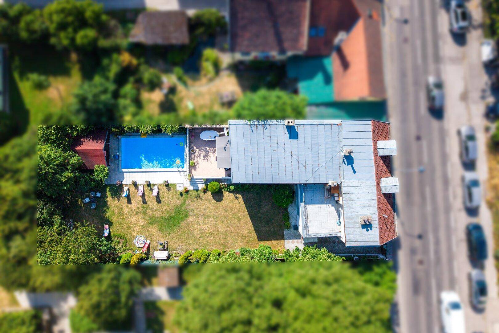 Luftaufnahme des Anwesens mit Haus, Pool, Garten und angrenzender Straße.