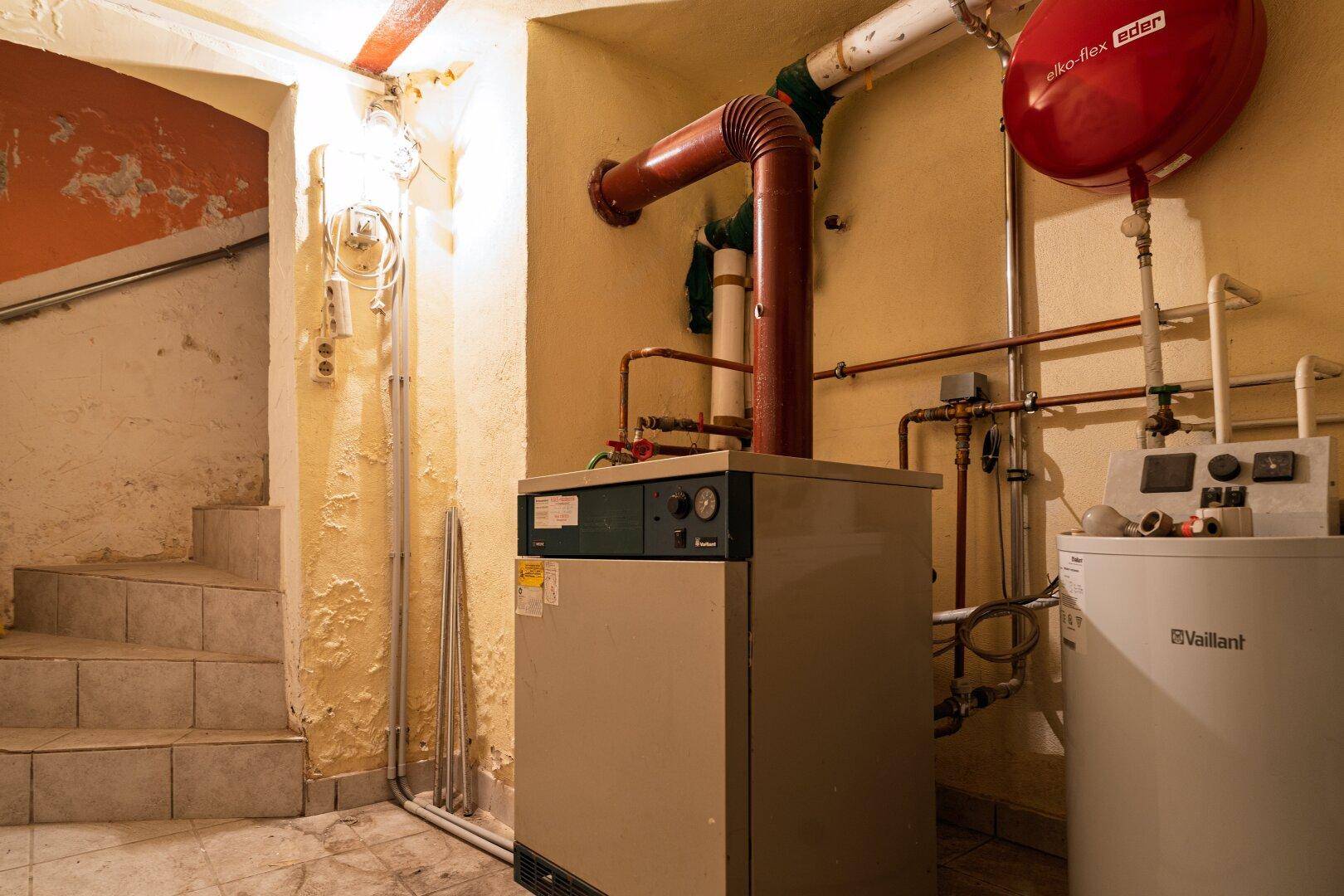 Kellerraum mit Heizungsanlage, Warmwasserspeicher und Treppenaufgang, zeigt den Versorgungsbereich.