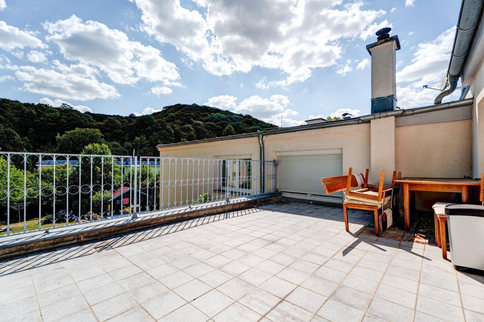 Geräumige Dachterrasse mit Metallgeländer und weitem Blick auf bewaldete Hügel.
