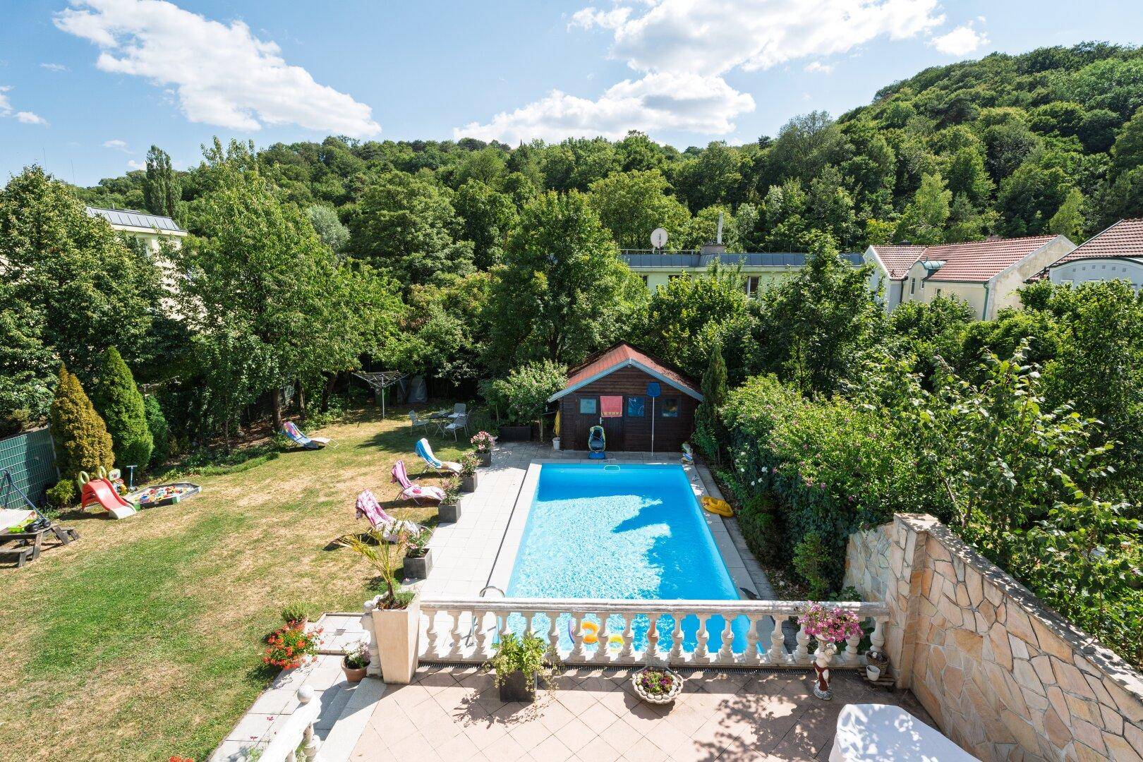 Großer Garten mit Swimmingpool, Liegestühlen und einem kleinen Gartenhaus, umgeben von viel Grün.