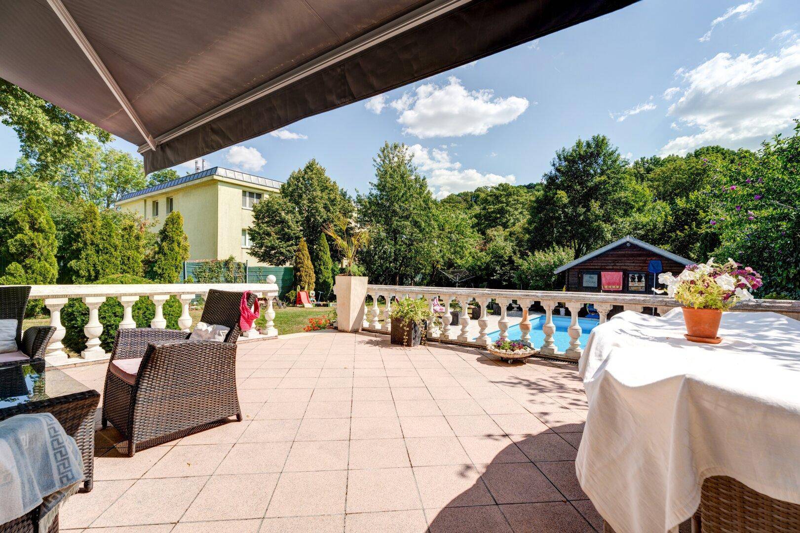 Große geflieste Terrasse mit Gartenmöbeln, Markise und weitem Blick ins Grüne.