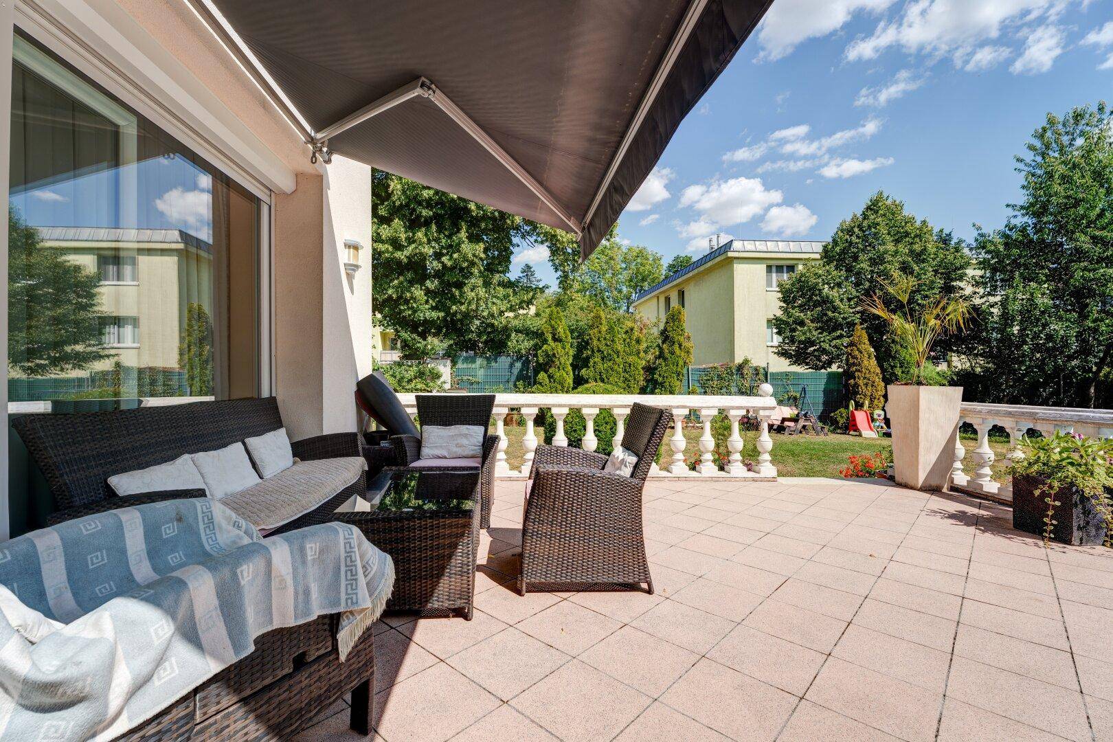 Gemütliche Terrasse mit Rattanmöbeln und ausfahrbarer Markise, umgeben von viel Grün.
