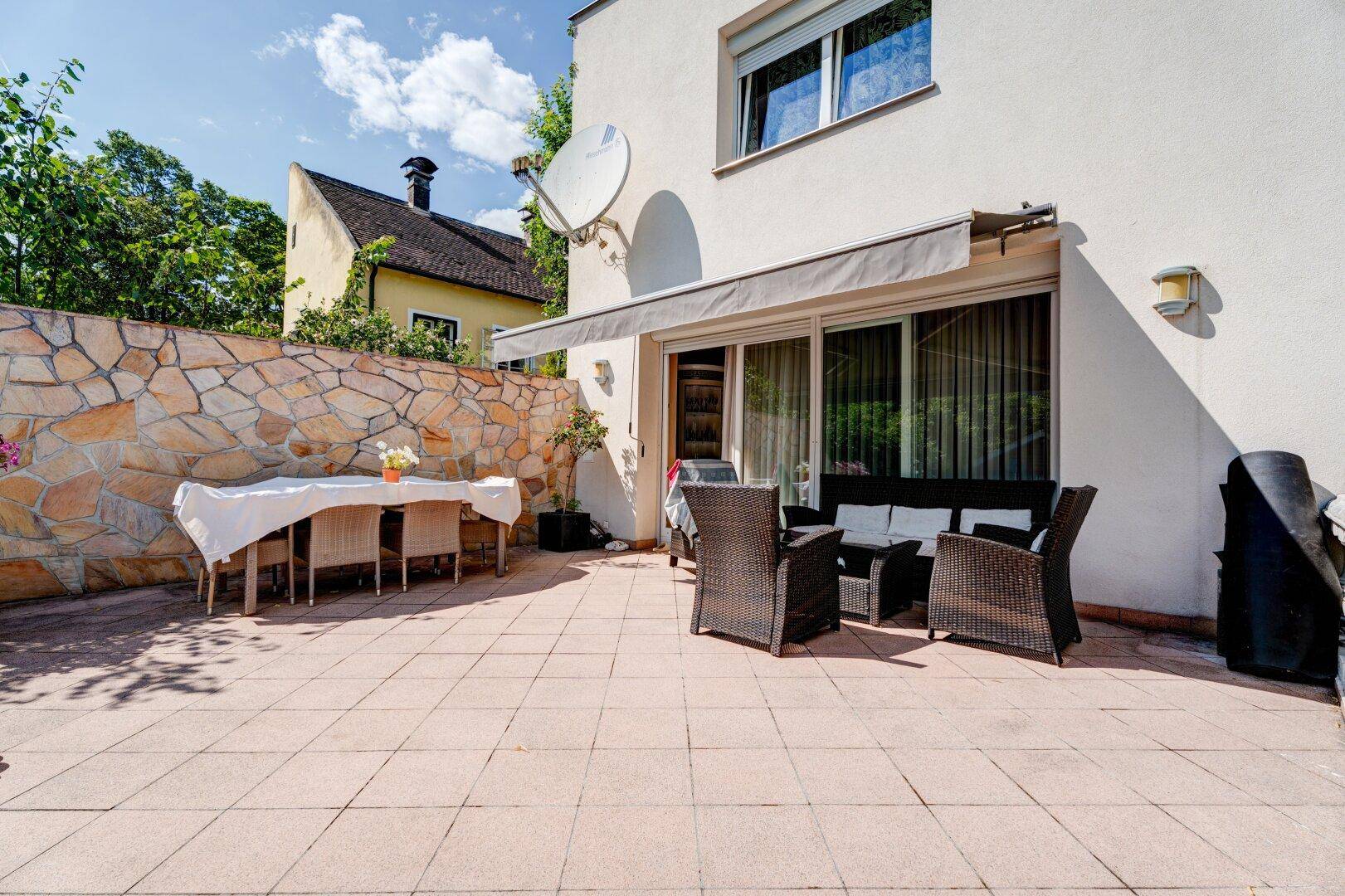 Große geflieste Terrasse mit Ess- und Lounge-Bereich, umgeben von einer Natursteinmauer.