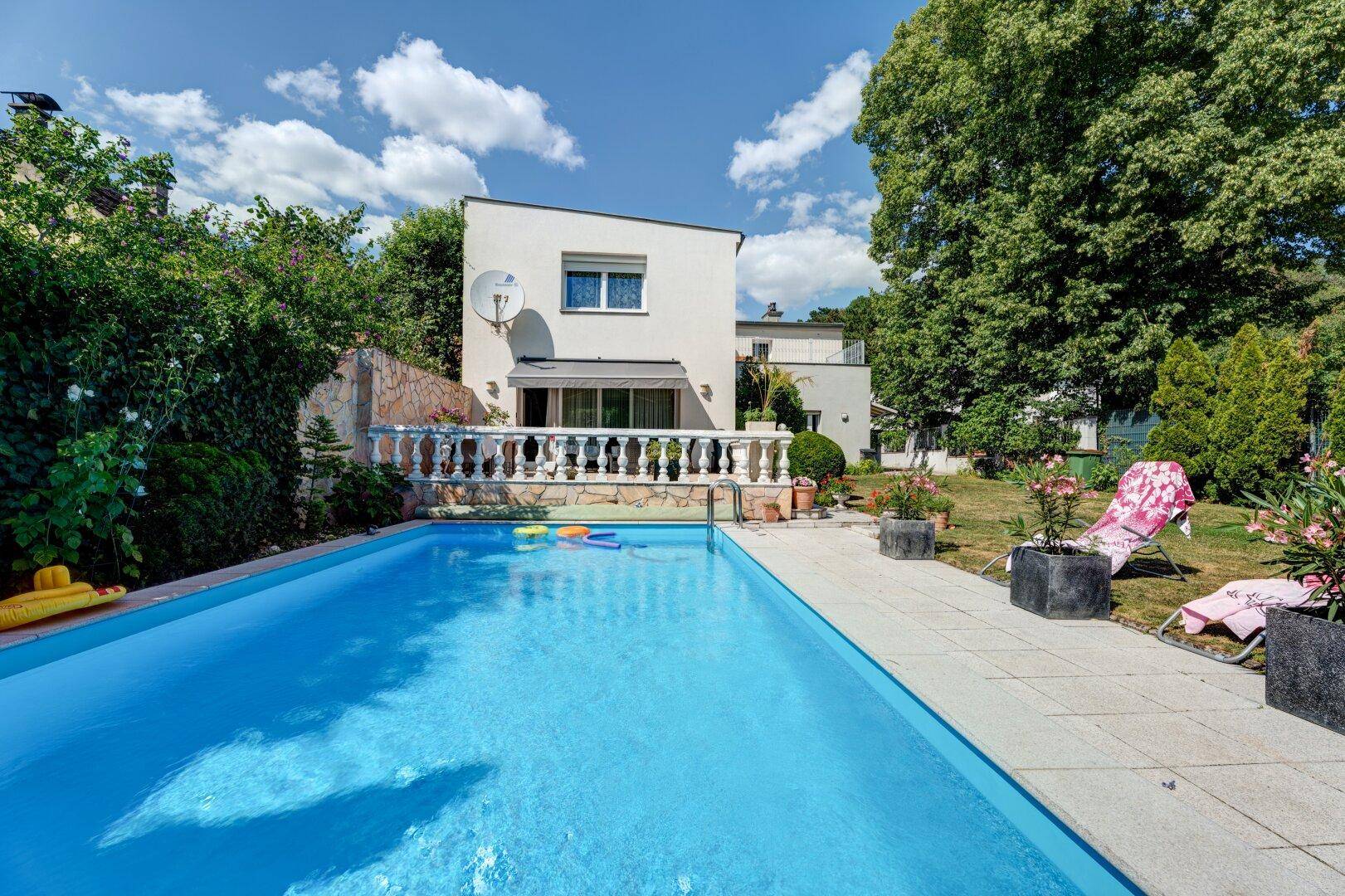 Außenpool mit gefliester Poolumrandung und Blick auf die Hausfassade unter blauem Himmel.