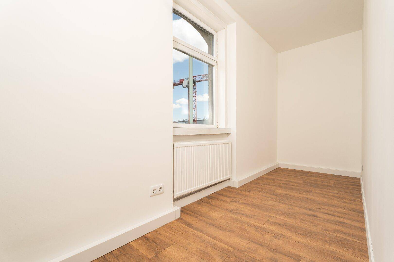 Helles Schlafzimmer mit Laminatboden und einem Fenster, das viel Tageslicht bietet.