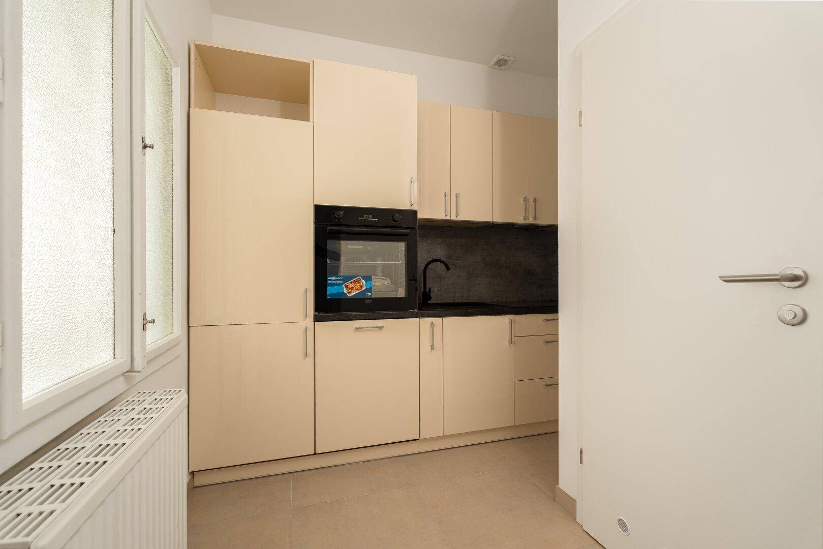 Funktionale Küche mit beigen Schränken, schwarzer Arbeitsplatte und Fenster für Tageslicht.