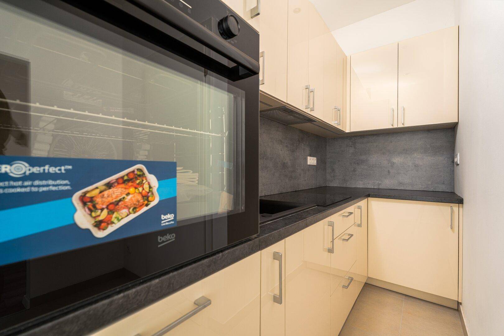 Detailansicht der Küche mit integriertem Backofen, Kochfeld und dunkler Arbeitsplatte.