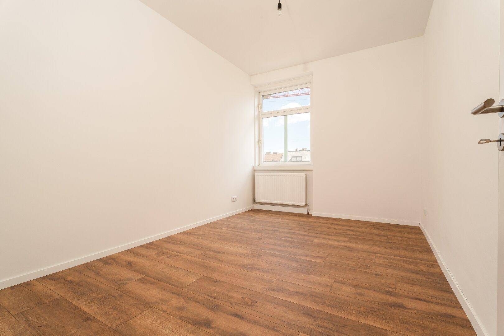 Geräumiges Schlafzimmer mit Laminatboden, weiß gestrichenen Wänden und einem Fenster.