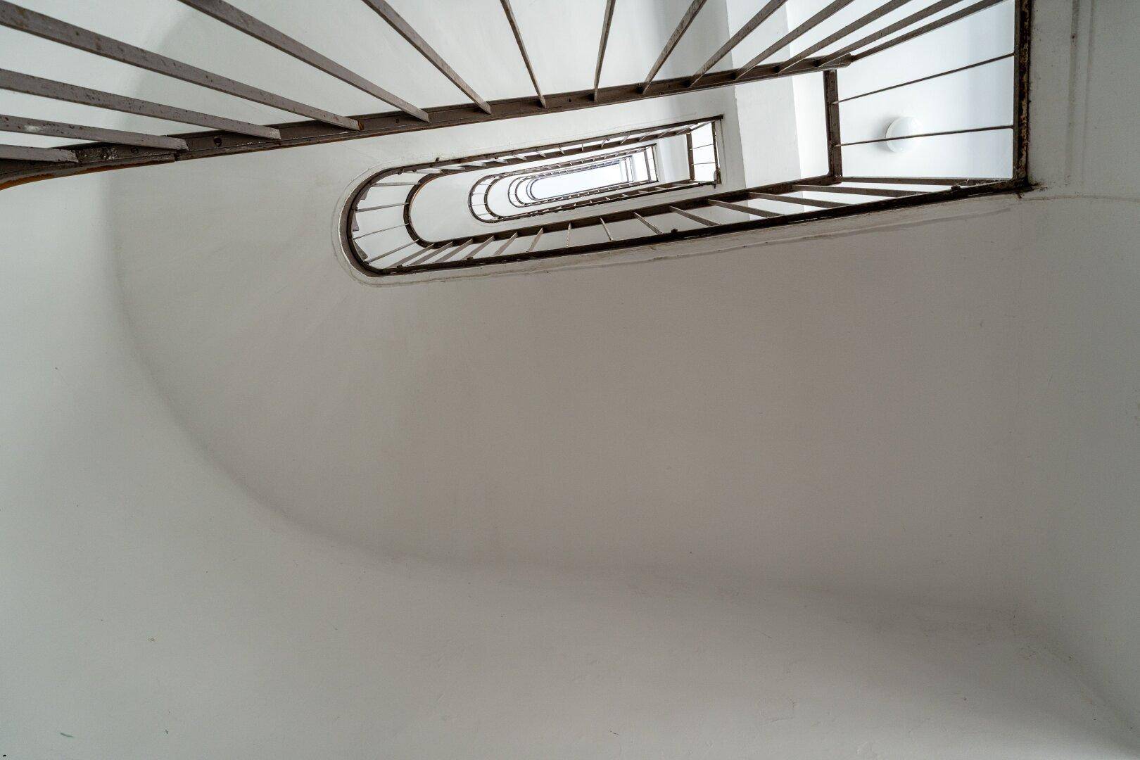 Blick von oben in ein Treppenhaus mit geschwungenen Stufen und Metallgeländer.