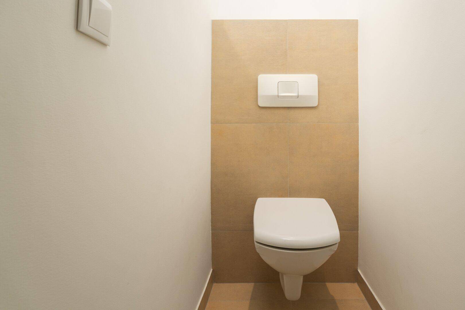 Separates WC mit wandhängender Toilette und beigefarbenen Fliesen an der Wand.
