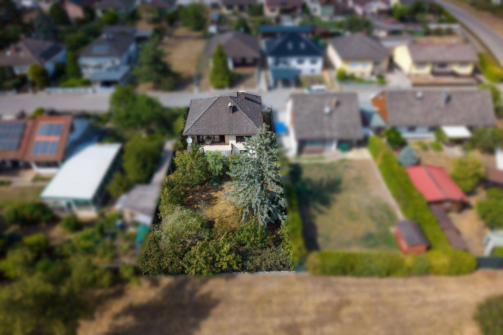 Übersichtliche Luftaufnahme eines Einfamilienhauses mit großem, naturbelassenem Gartenbereich.