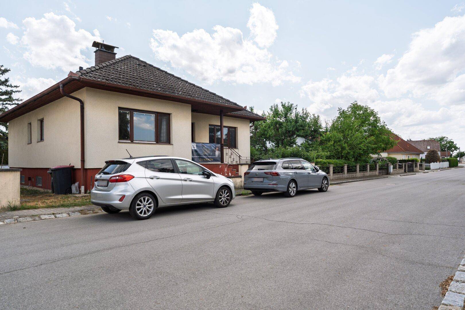 Seitenansicht des Hauses von der Straße mit geparkten Fahrzeugen.