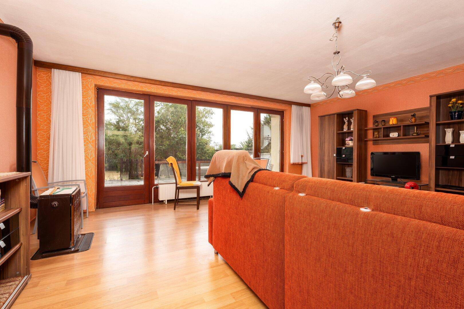 Helles Wohnzimmer mit großen Fenstern, Holzboden und einem Holzofen.