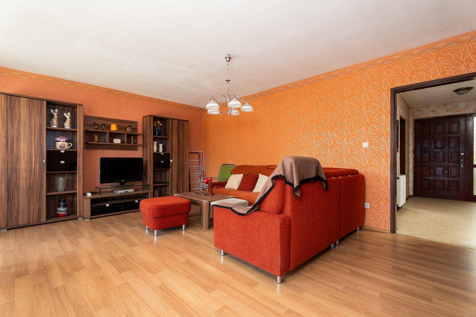 Wohnzimmer mit orangefarbener Tapete, Holzmöbeln und Parkettboden.