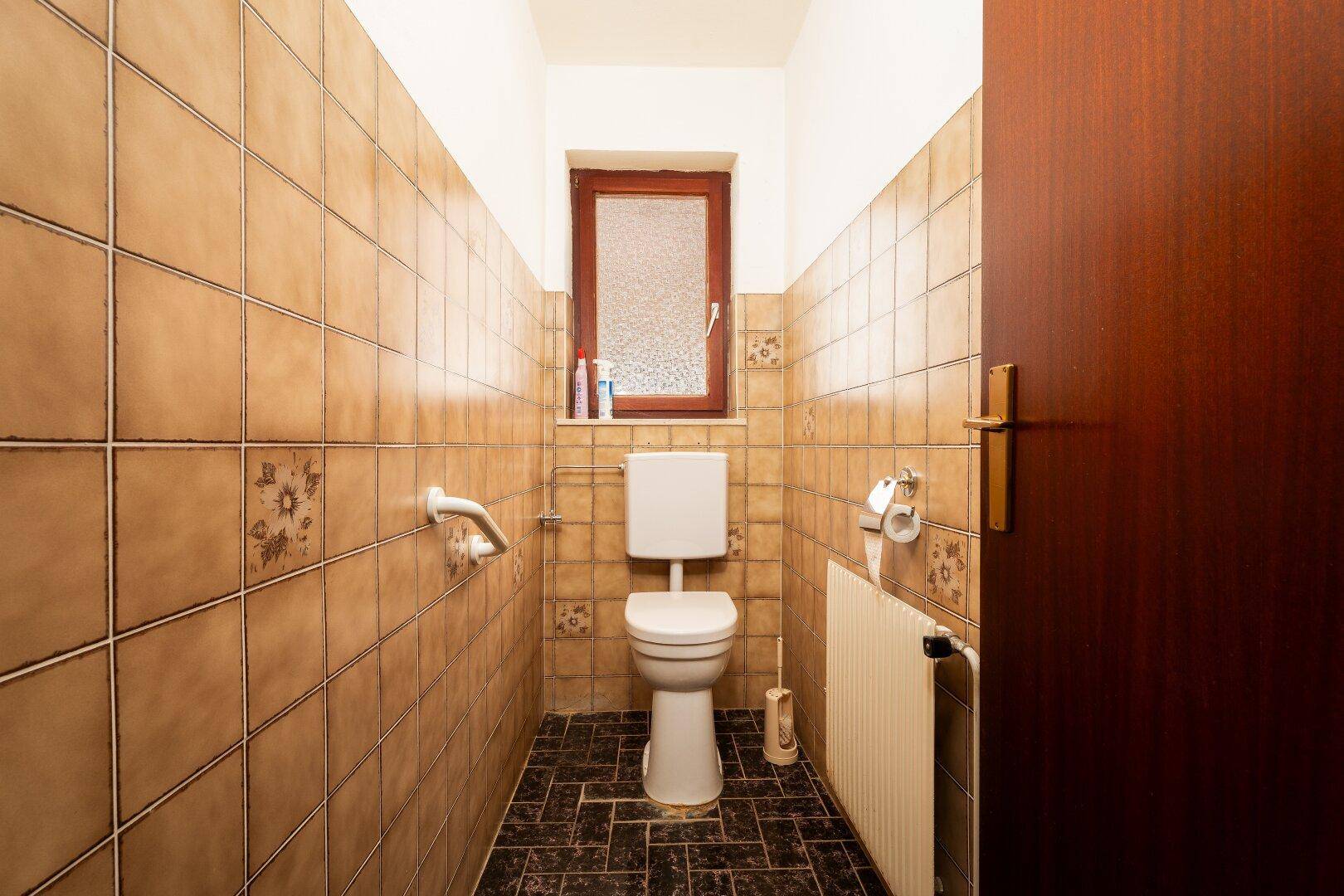 Separate Toilette mit WC, Fenster und beigefarbenen Fliesen.