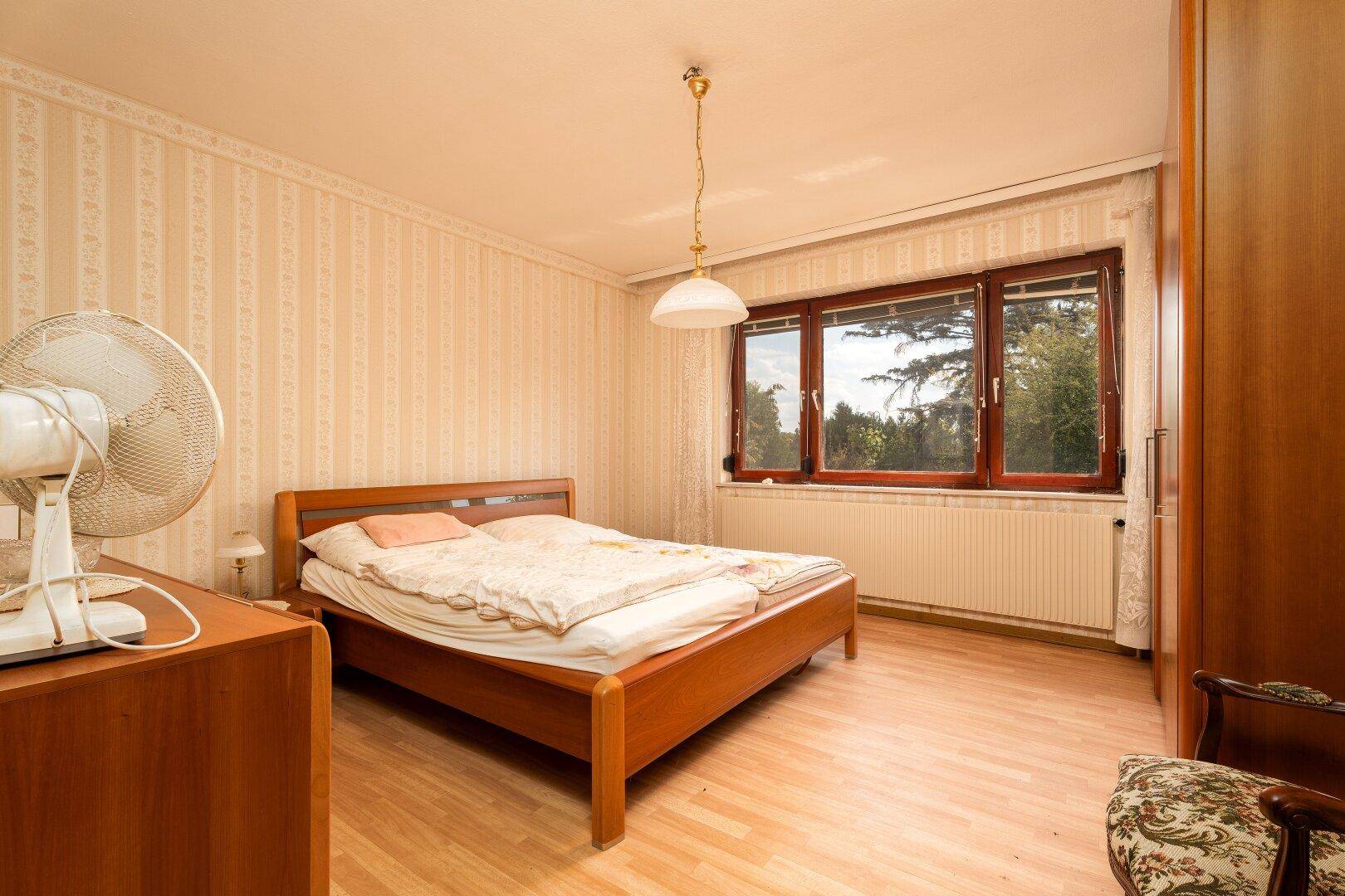 Schlafzimmer mit Doppelbett, Holzmöbeln, gemusterter Tapete und Fenster.