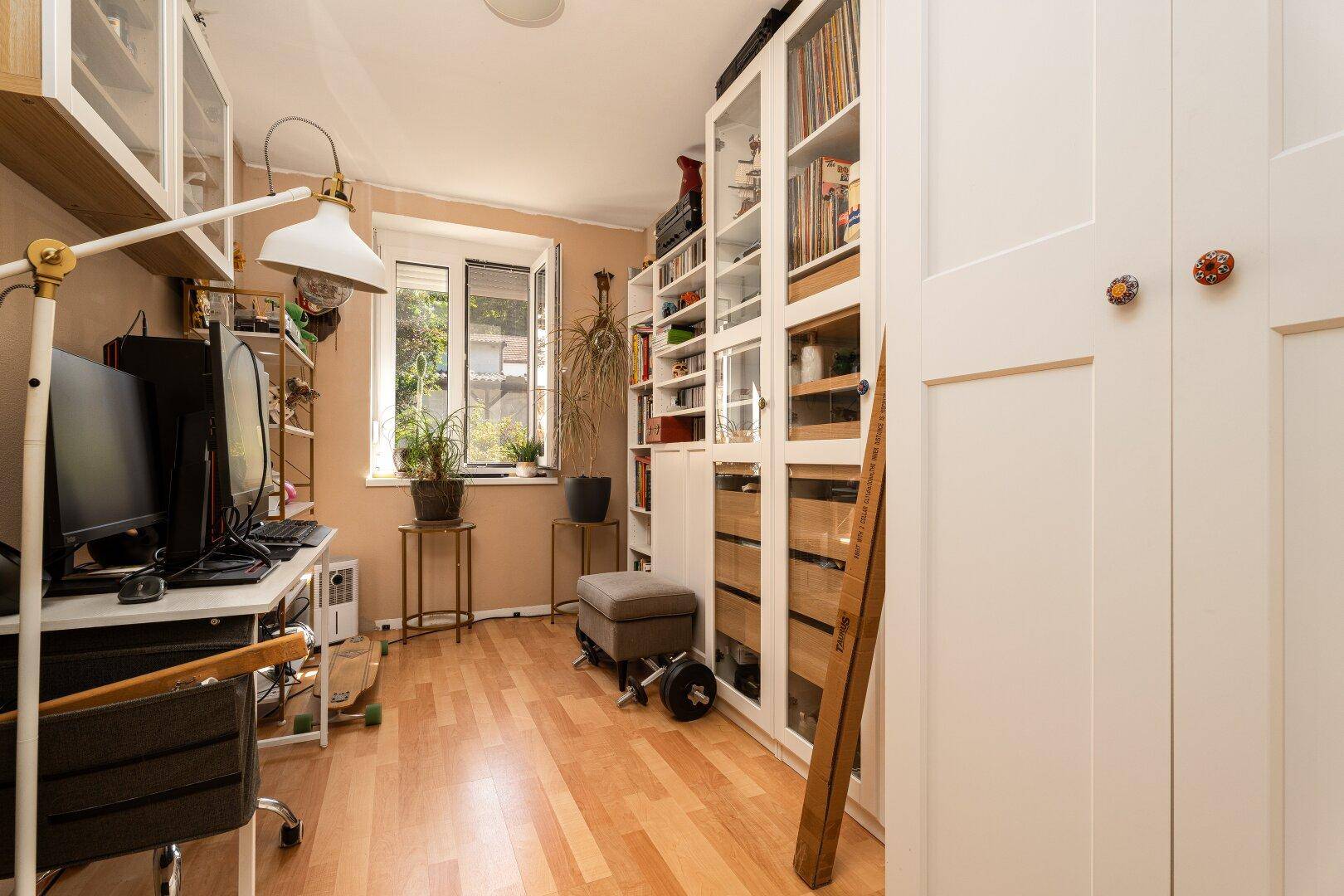 Helles Arbeitszimmer mit Laminatboden, Bücherregalen und einem Schreibtisch am Fenster.