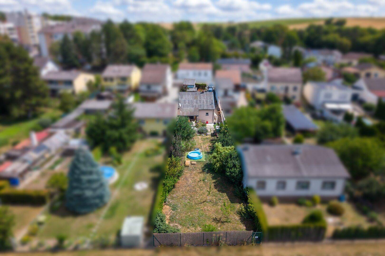 Luftaufnahme eines Grundstücks mit langem Garten, kleinem Pool und umliegenden Häusern und Feldern.