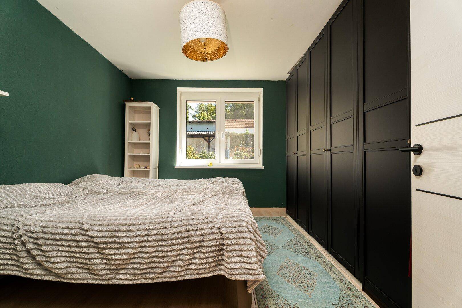 Gemütliches Schlafzimmer mit grüner Wandfarbe, Laminatboden und einem Fenster mit Blick ins Grüne.