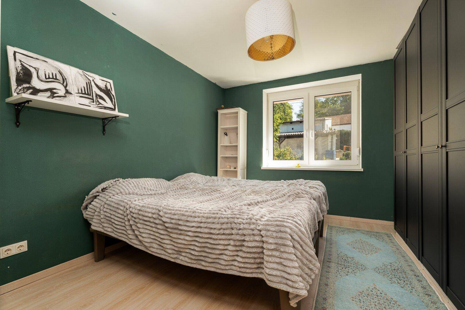 Schlafzimmer mit dunkelgrünen Wänden, Laminatboden und einem großen Kleiderschrank.