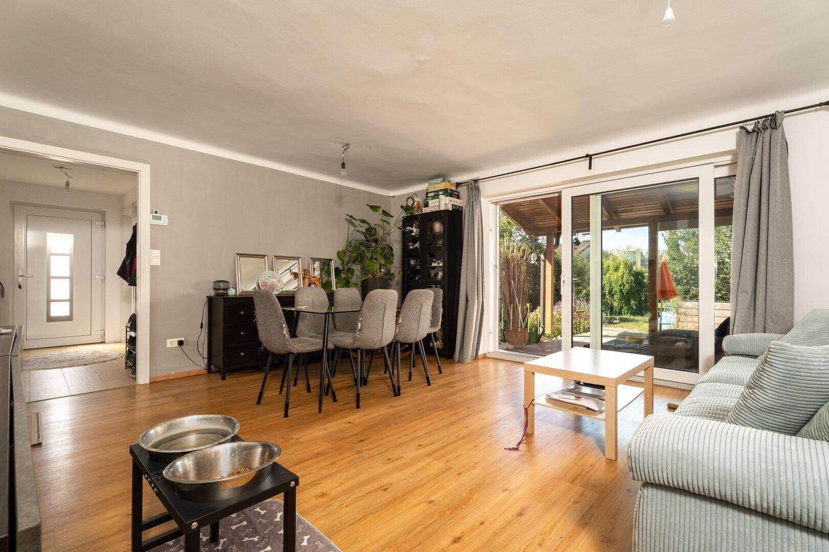 Heller Wohn-Essbereich mit Laminatboden, Esstisch und Zugang zur überdachten Terrasse.
