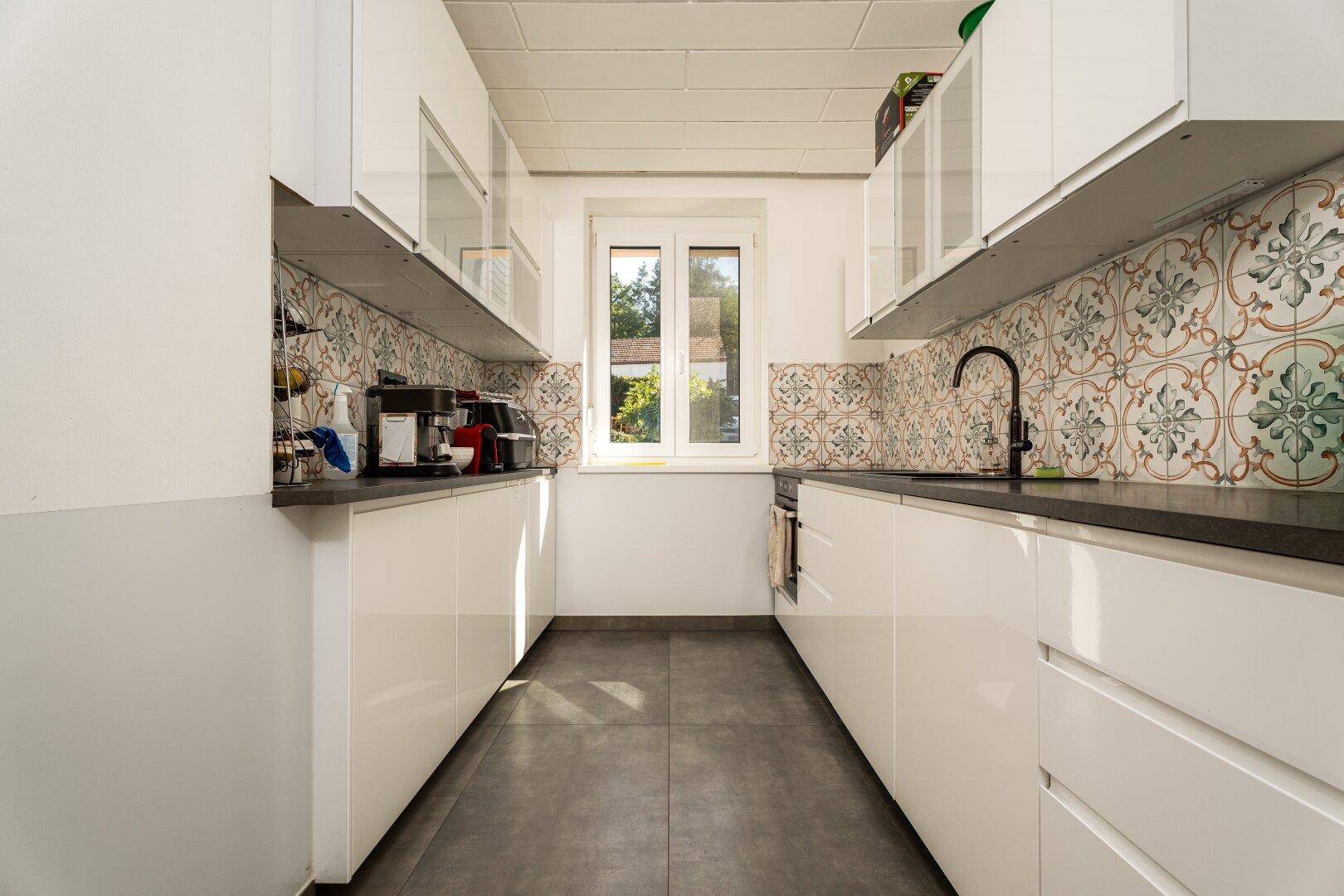 Moderne Küche mit weißen Hochglanzfronten, dunkler Arbeitsplatte und gemusterten Fliesen.
