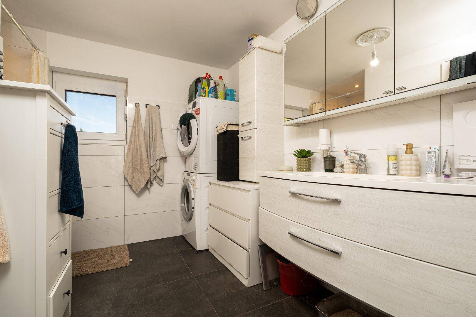 Helles Badezimmer mit Waschmaschine, Trockner und Doppelwaschbecken unter Spiegelschränken.