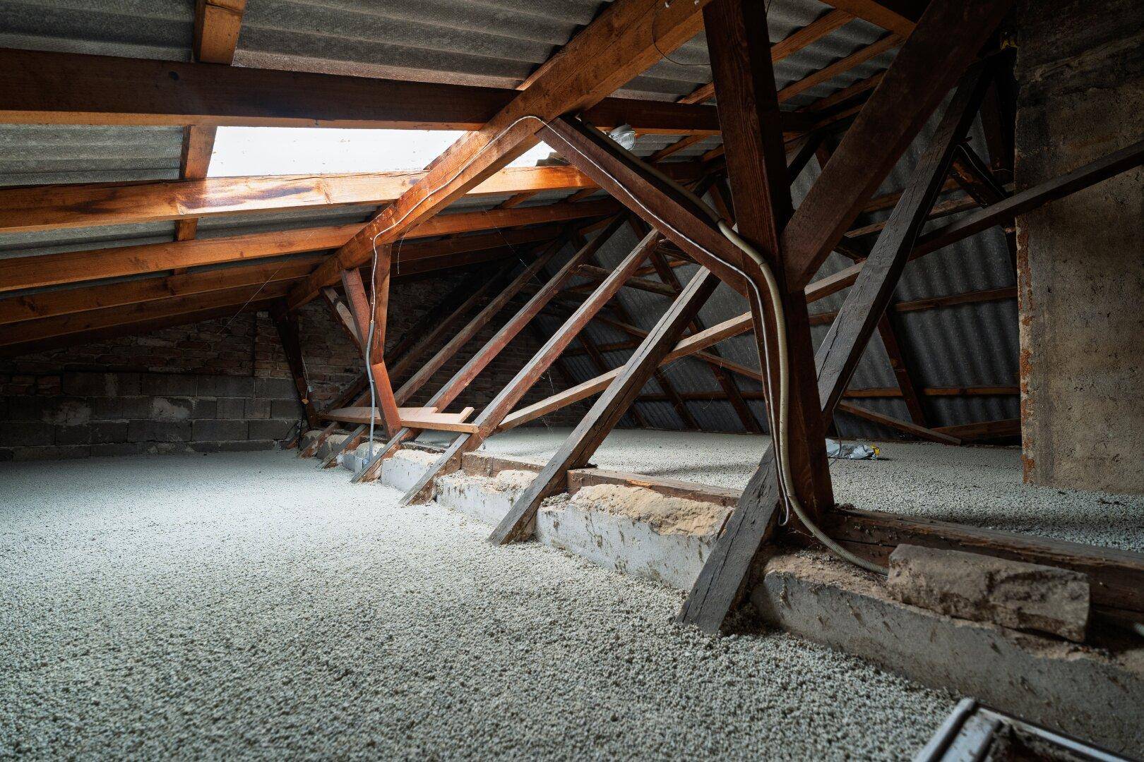Unausgebauter Dachboden mit sichtbarer Holzkonstruktion und Dämmmaterial auf dem Boden.