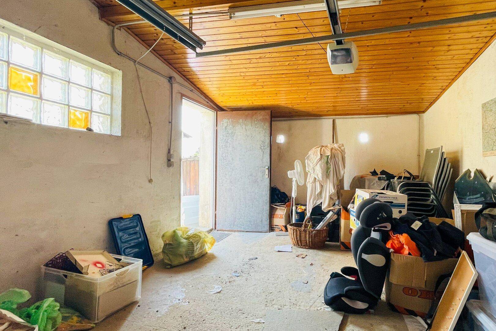 Garage mit Holztür, Glasbausteinfenster und viel Platz für Lagerung und Werkstatt.