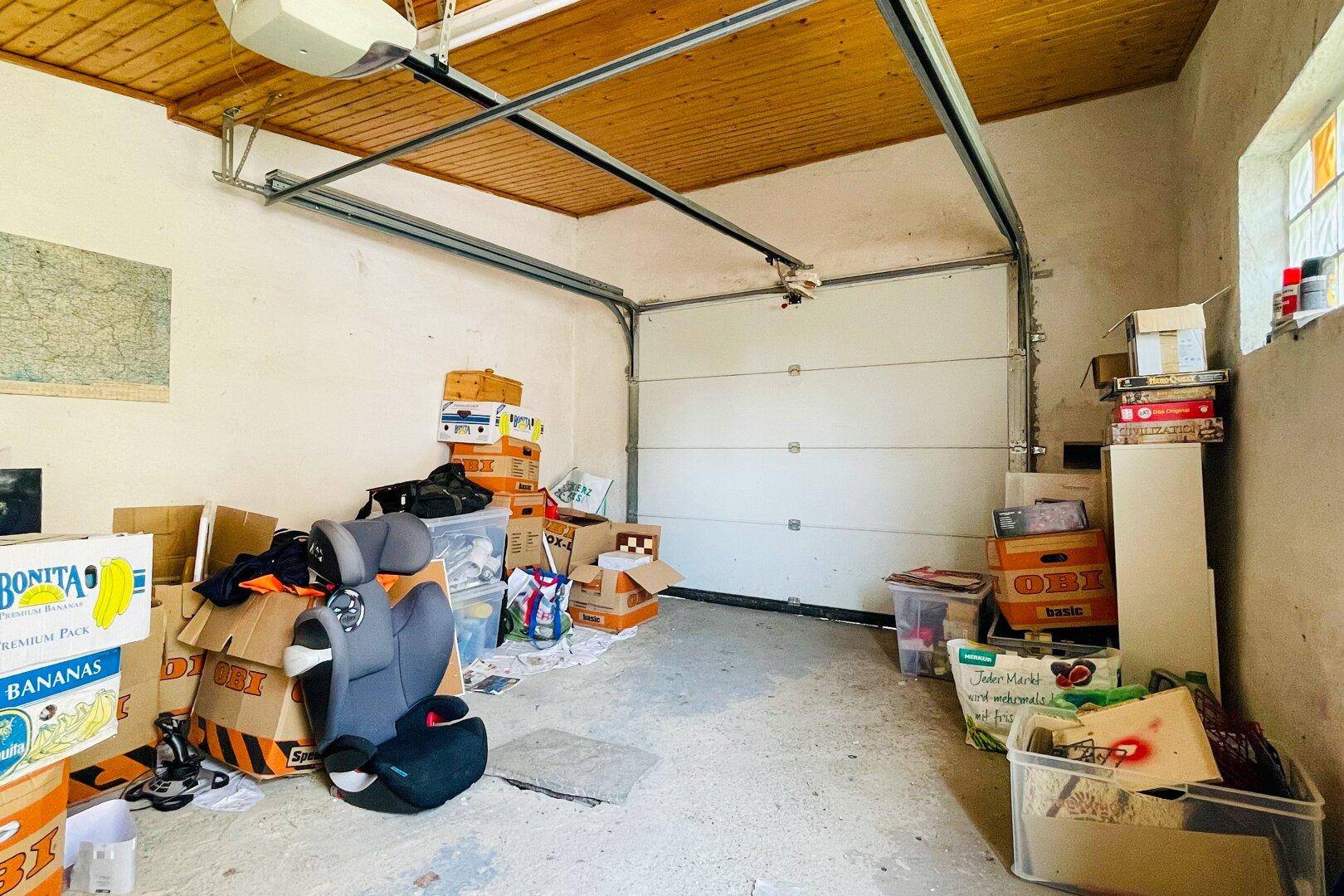 Geräumige Garage mit Sektionaltor, Holzdecke und viel Stauraum für diverse Gegenstände.
