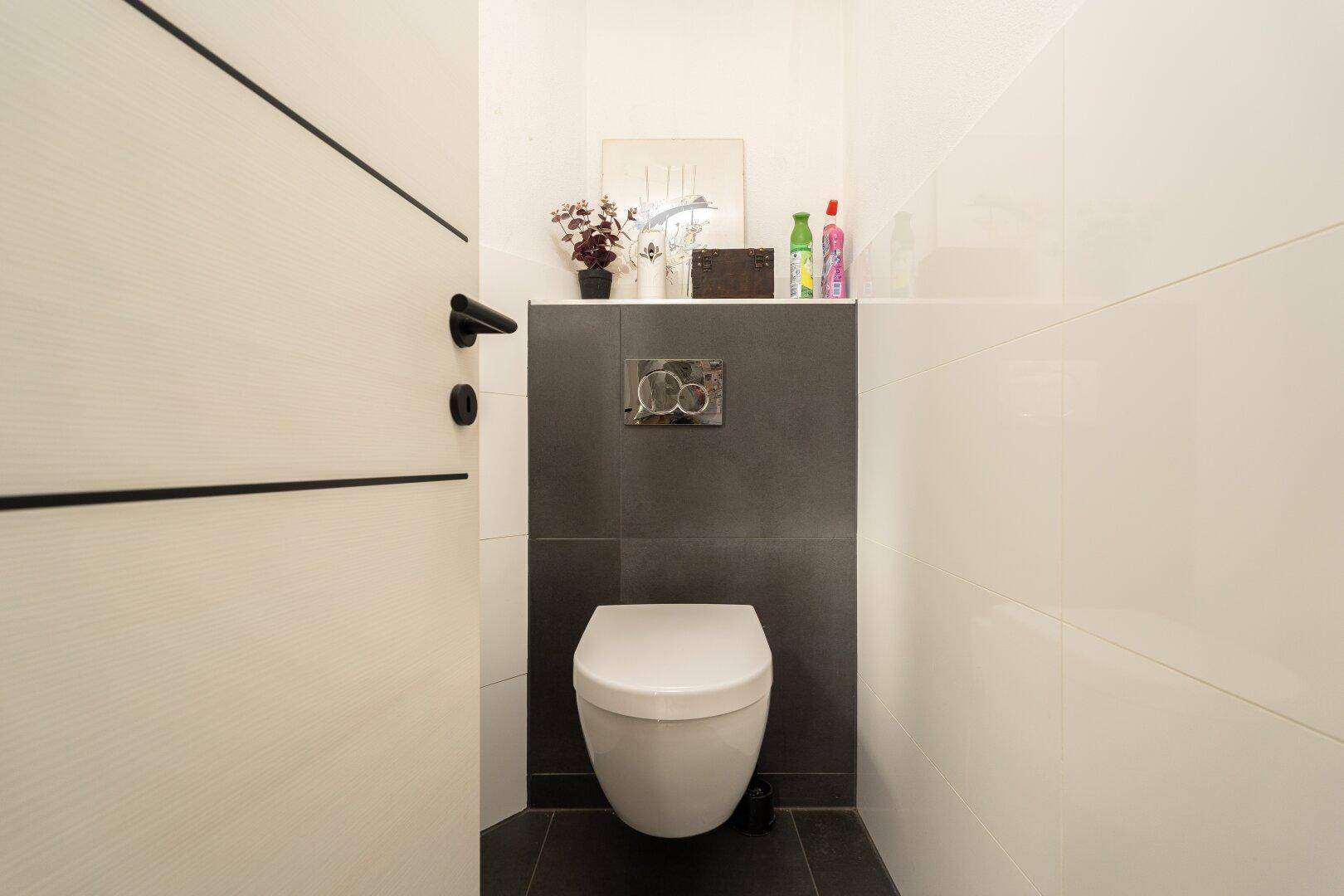 Modernes Gäste-WC mit wandhängendem WC und dunklen sowie weißen Fliesen.
