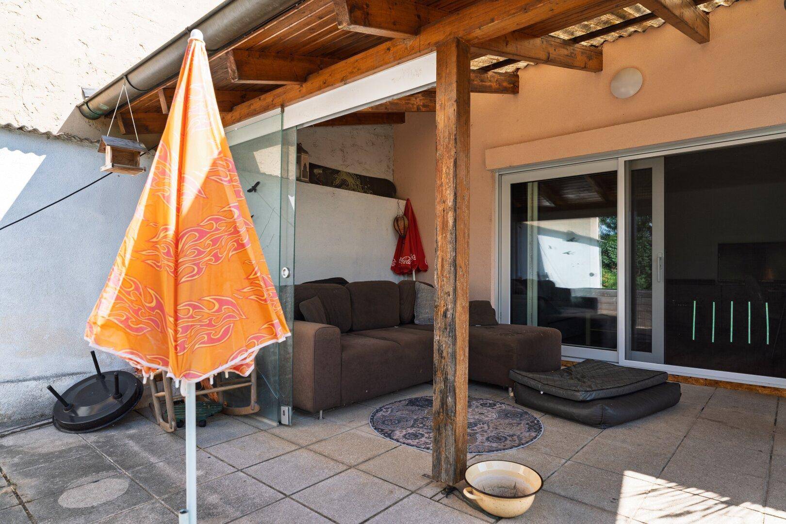 Gemütliche überdachte Terrasse mit Fliesenboden, Loungemöbeln und großem Sonnenschirm.