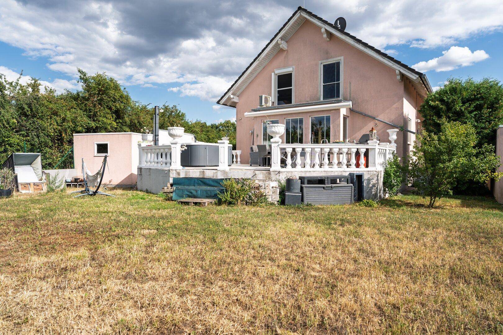 Gartenansicht des Hauses mit Rasenfläche und einer großzügigen Terrasse mit Balustrade.