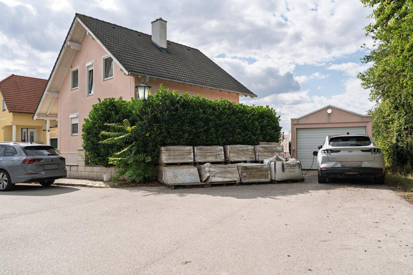 Vorderansicht des Hauses von der Straße mit Garage und geparkten Fahrzeugen.