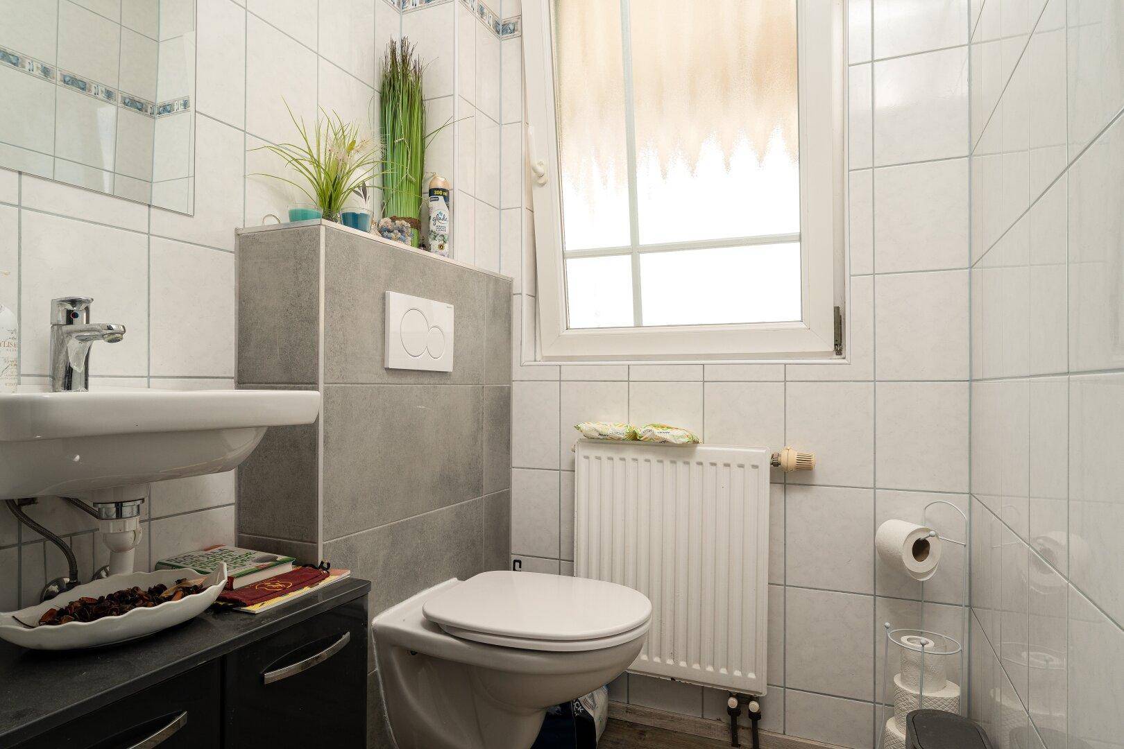 Kleines Gäste-WC mit weißen Fliesen, wandhängendem WC und Fenster für Tageslicht.