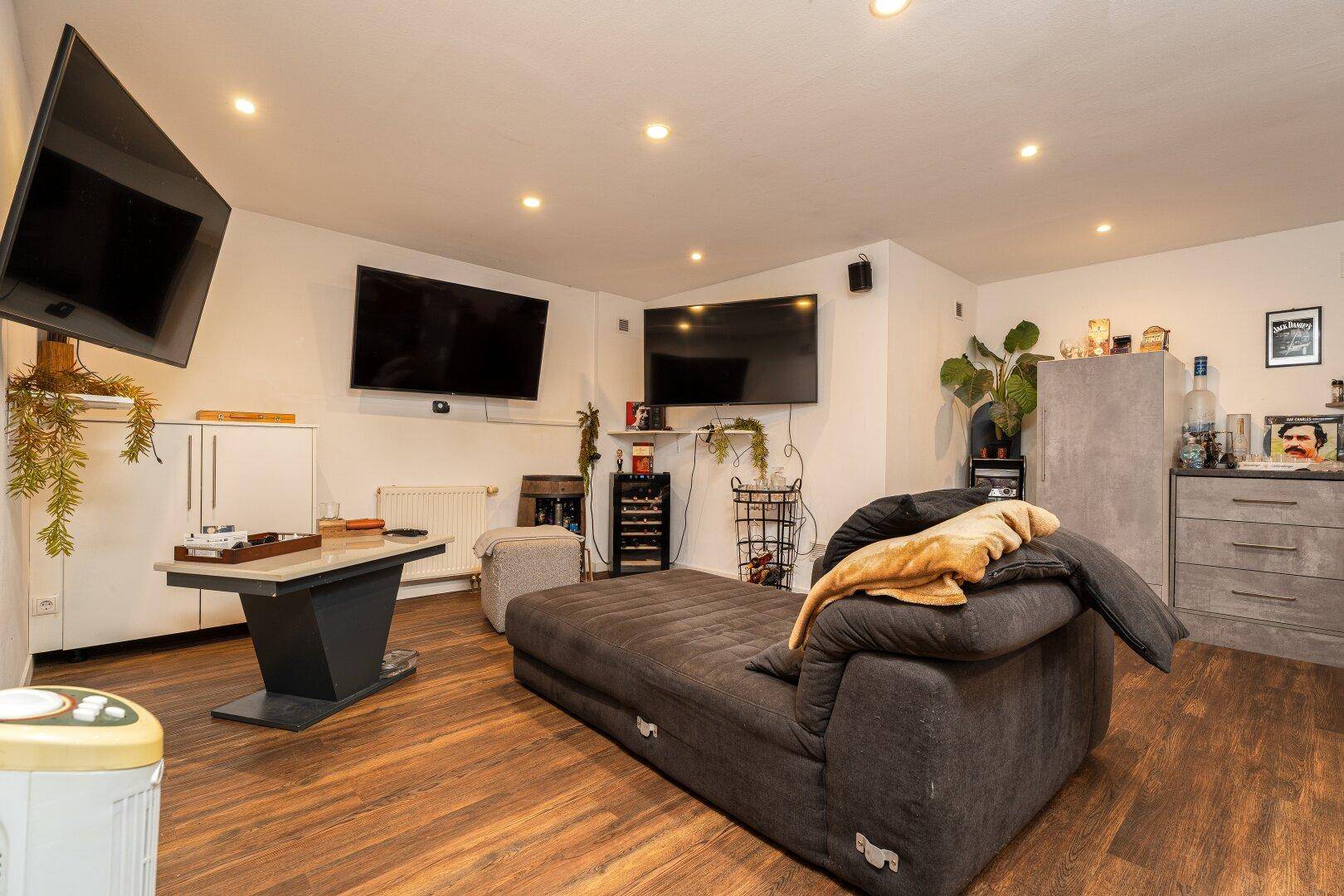 Geräumiges Wohnzimmer mit bequemer Couch, mehreren Fernsehern und modernem Dekor.