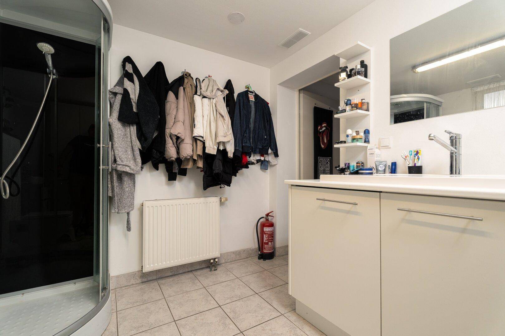 Badezimmer mit Waschtisch, Duschkabine und Heizkörper, auch als Garderobe genutzt.