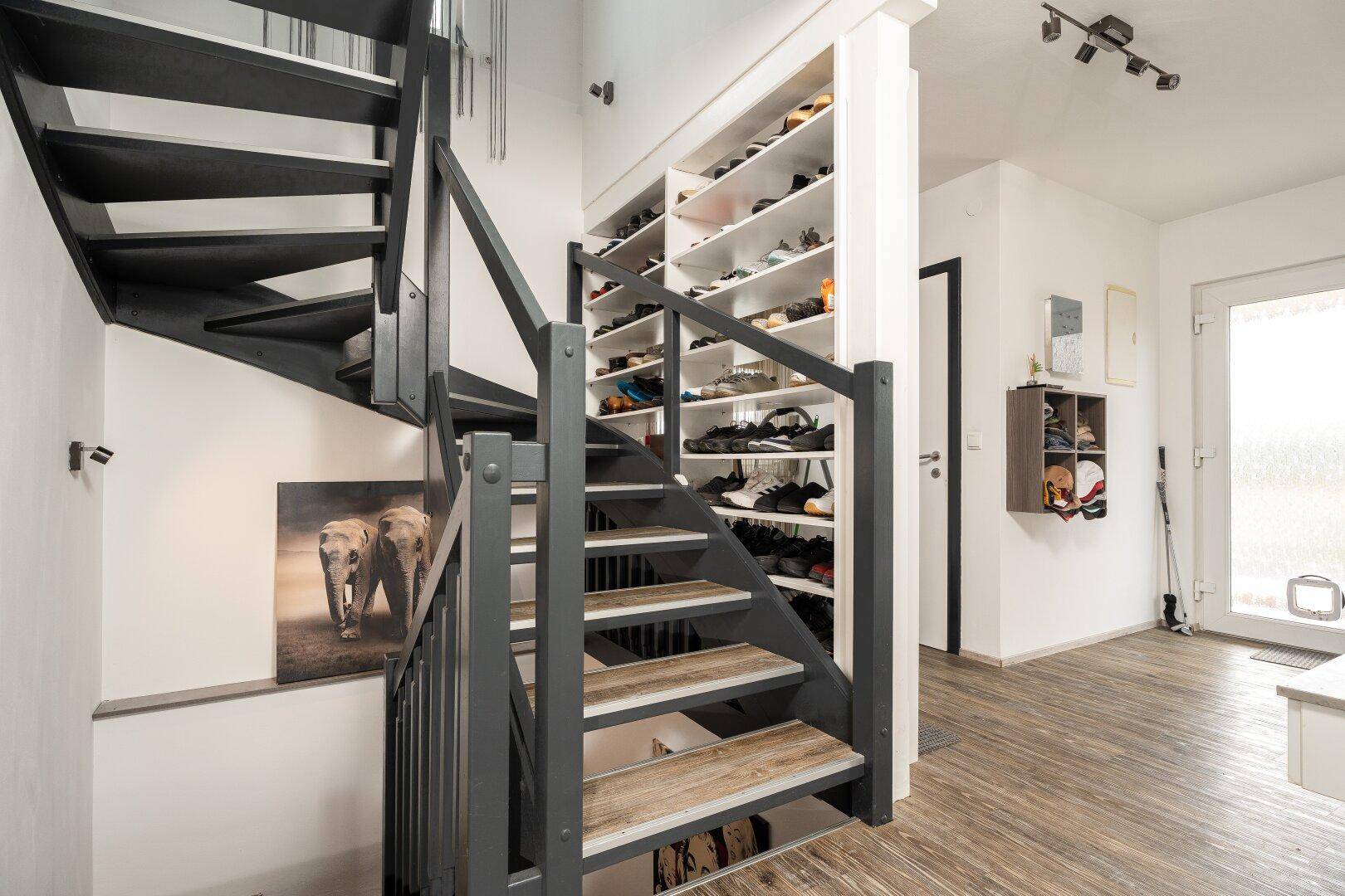 Moderne Treppe mit dunklem Geländer und integriertem Schuhregal im Flurbereich.